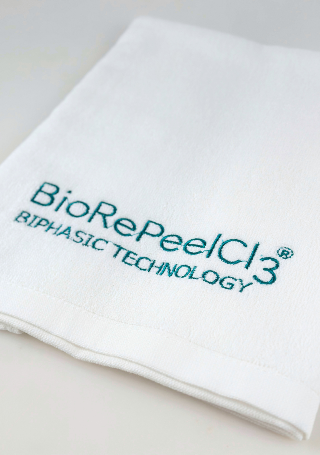 TOWEL BIOREPEEL SMALL, WHITE WITH BLUE-TO-GREEN LOGO 
40x60 cm Malý bavlnený uterák s logom BioRePeel, biely s tyrkysovou výšivkou