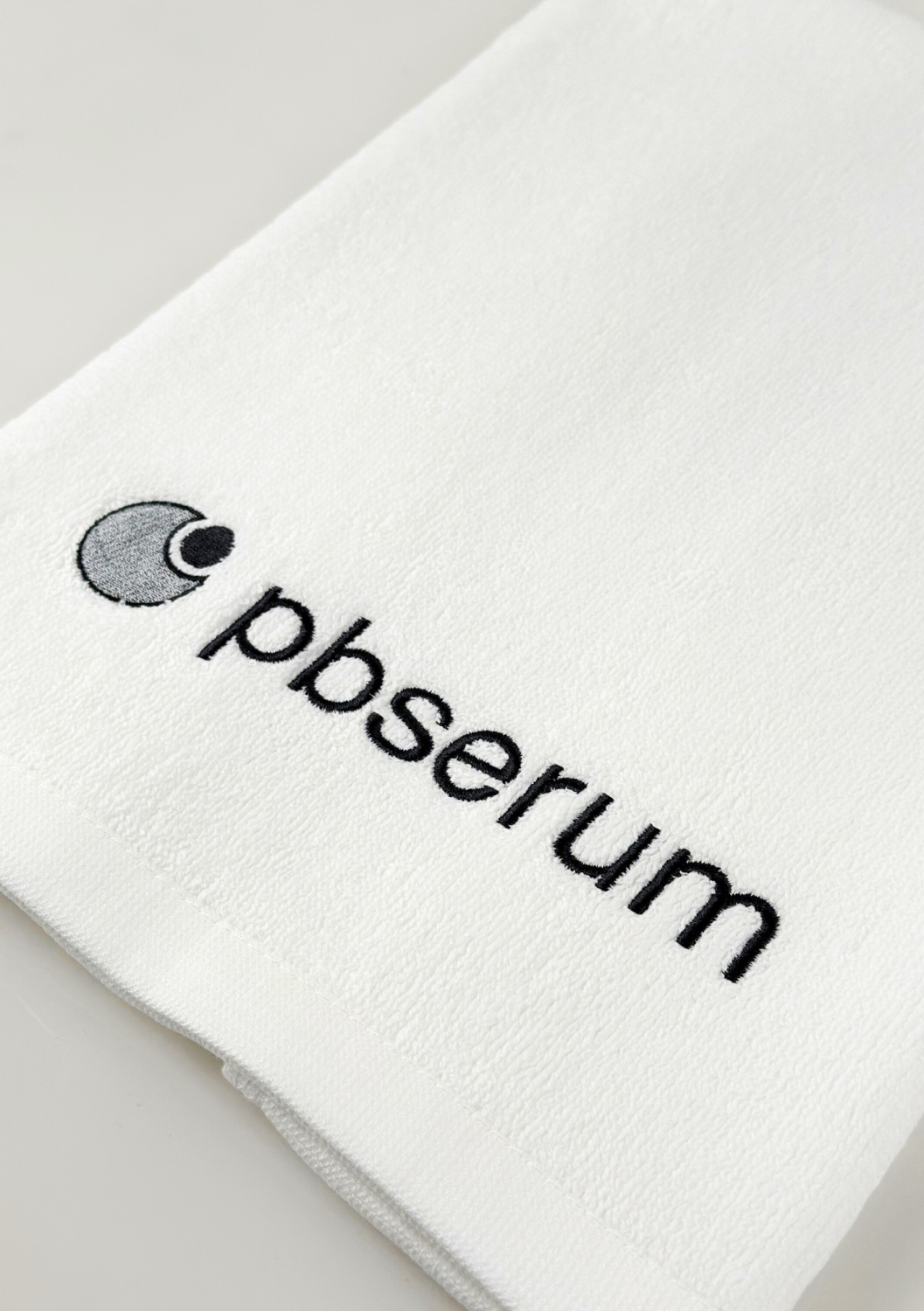 TOWEL PBSERUM SMALL, WHITE WITH GREY LOGO 
40x60 cm Kleines Baumwollhandtuch mit PBSerum-Logo, weiß mit grauer Stickerei